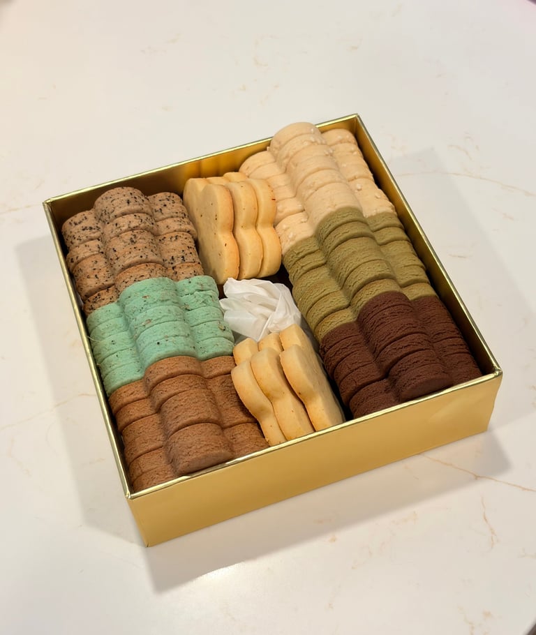 Assorted cookies and crackers arranged in a gold box, including chocolate chip, pistachio, vanilla wafer, and brown butter varieties